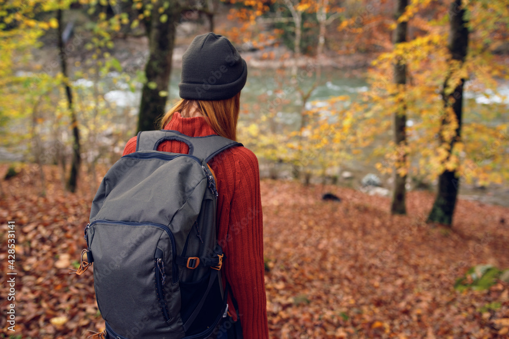 woman in a sweater with a backpack on her back near the river in the mountains and park trees autumn landscape