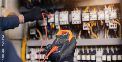 Electrician engineer work tester measuring voltage and current of power electric line in electical cabinet control.and wires on relay protection system. Bay control unit. Medium voltage switchgear. © A Stockphoto