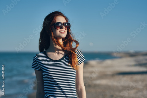 portrait of a beautiful traveler with glasses red hair t-shirt beach summer landscape sea