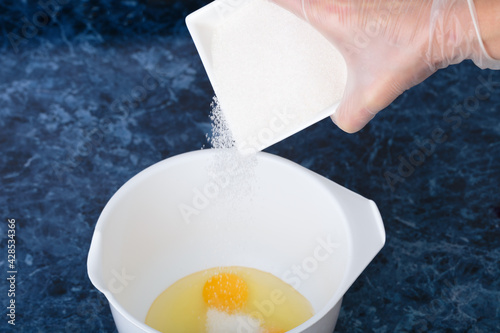 Pour sugar into a bowl with broken eggs.