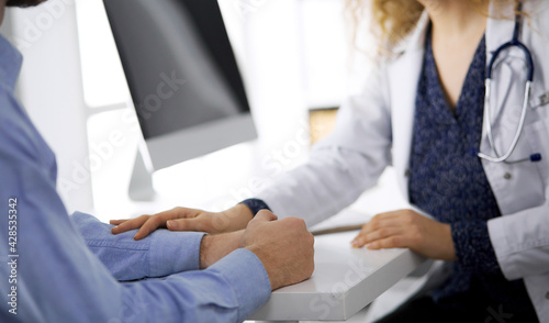 Female doctor and male patient discussing current health examination while sitting in clinic  close-up. Medicine concept