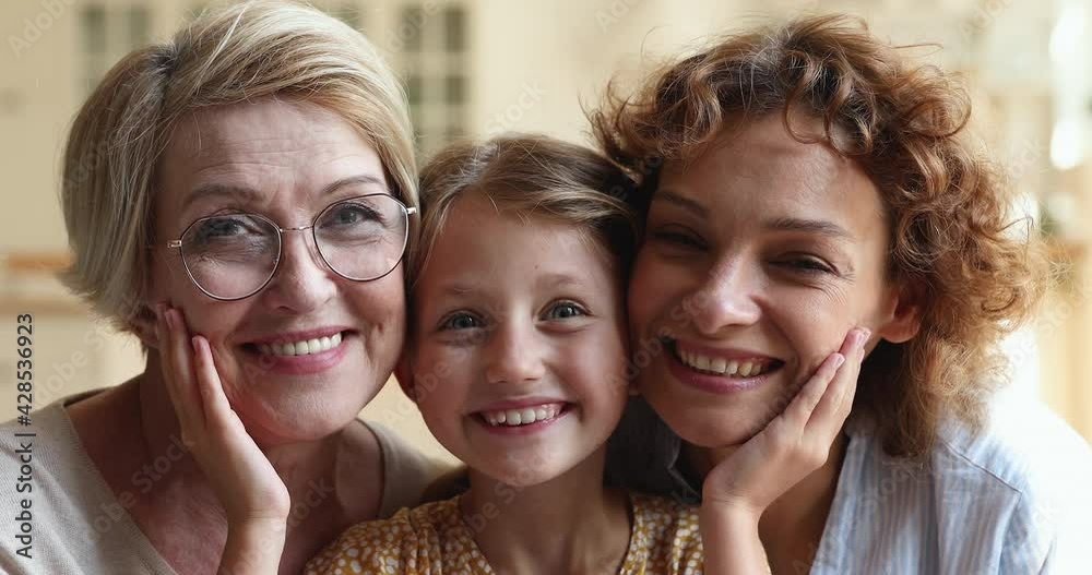Three generations of relatives beautiful women, multi-generational family close up portrait concept, cute girl grandkid posing between 60s granny and loving mother smiling for camera laughs feel happy