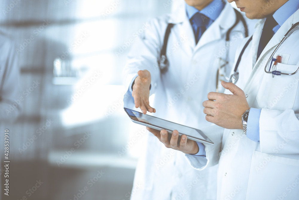 Group of unknown doctors use a computer tablet to check up some medical names records, while standing in a hospital office. Physicians ready to examine and help patients. Medical help, insurance in Group of unknown doctors use a computer tablet to check up some medical names records, while standing in a hospital office. Physicians ready to examine and help patients. Medical help, insurance in