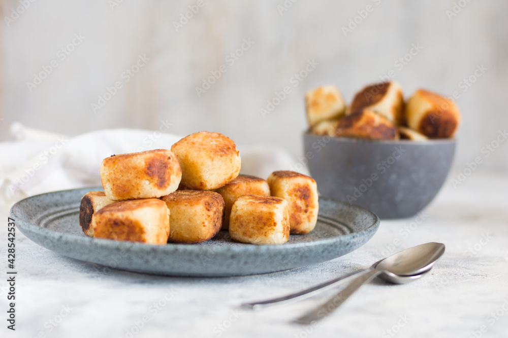 Square curd pancakes, traditional Russian cheesecakes on a light background with cutlery. Square curd pancakes, traditional Russian cheesecakes on a light background with cutlery.