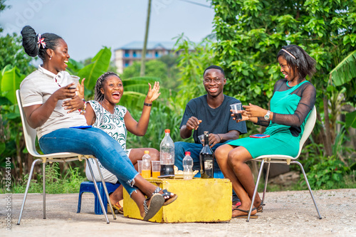 selective focus of african youth, with drinks and cups on yellow box- candid image of black ladies and a guy outdoor having fun- partying concept  © AMO