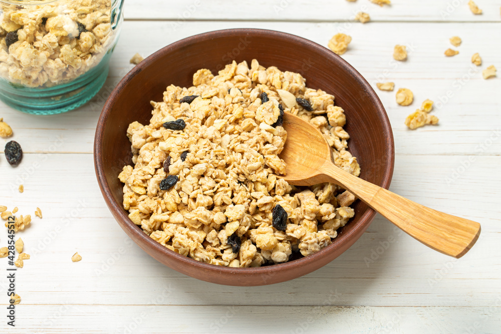 Healthy breakfast. Muesli with dried grapes in a clay bowl on a white wooden table. Muesli is scattered on the table. Healthy breakfast. Muesli with dried grapes in a clay bowl on a white wooden table. Muesli is scattered on the table.