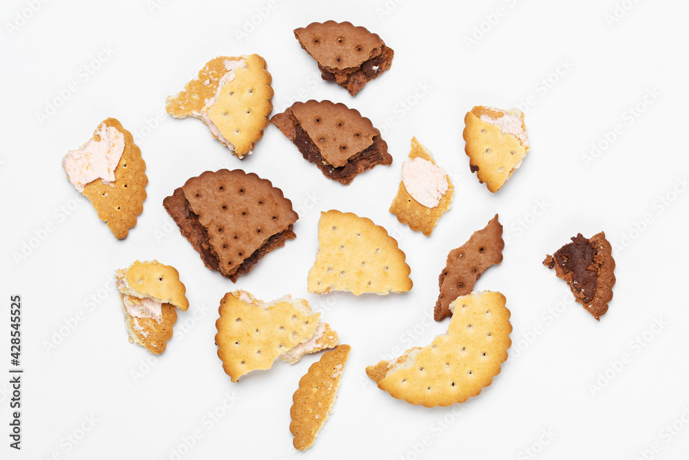 Pieces of chocolate chip cookies and biscuits with filling on a white plate close-up. Top view. Pieces of chocolate chip cookies and biscuits with filling on a white plate close-up. Top view.