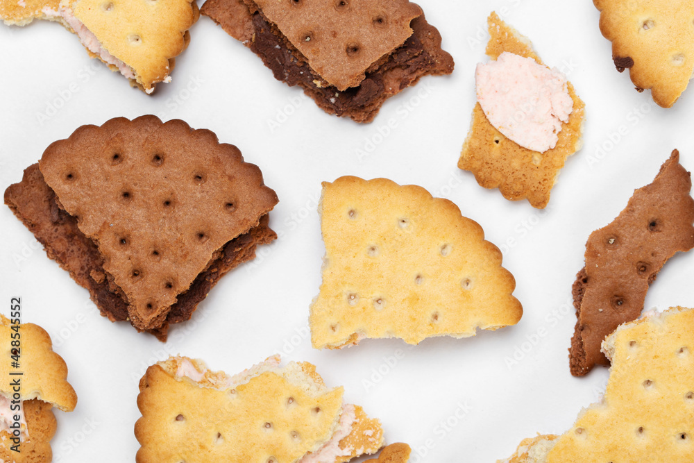 Pieces of chocolate chip cookies and biscuits with filling on a white plate close-up. Top view. Pieces of chocolate chip cookies and biscuits with filling on a white plate close-up. Top view.