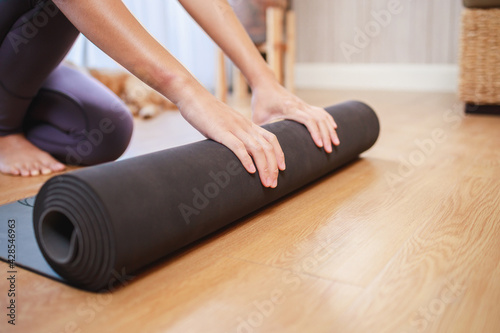 Close-up of woman hands unrolling roll black yoga mat for playing yoga at home