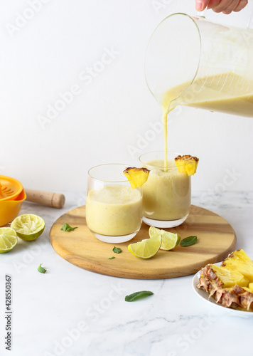 Vegan Pineapple smoothie on a wooden board. Ingredients: pineapple, banana, lime juice, soy yogurt. Healthy food concept, veganism and vegetarianism.