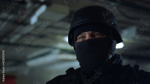 SWAT member standing in dark building. Masked military soldier posing at camera