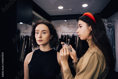 Make up talanted artist doing maquillage to woman applying concealer. Visagist using brushes shadows facial professional cosmetics for makeup. Beauty industry studio, image with copy space. photo