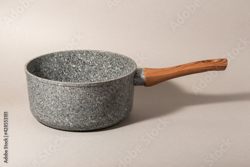Stone saucepan with wooden handle on solid background.