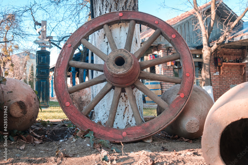 Wooden red wheel from an ancient cart standing in front of the tree at the yard