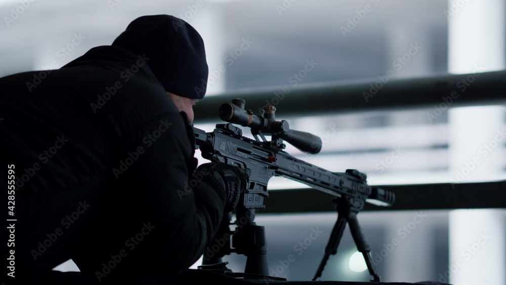 Hitman shooting with sniping rifle. Serious killer targeting scope on weapon