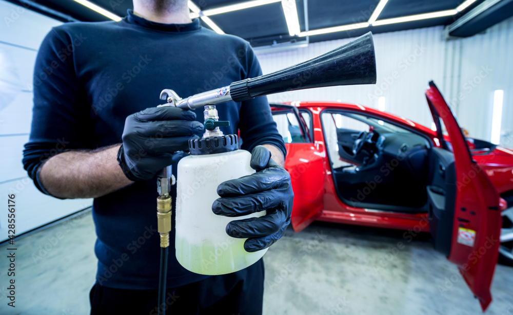 A car service worker cleans interiror with a special foam generator A car service worker cleans interiror with a special foam generator