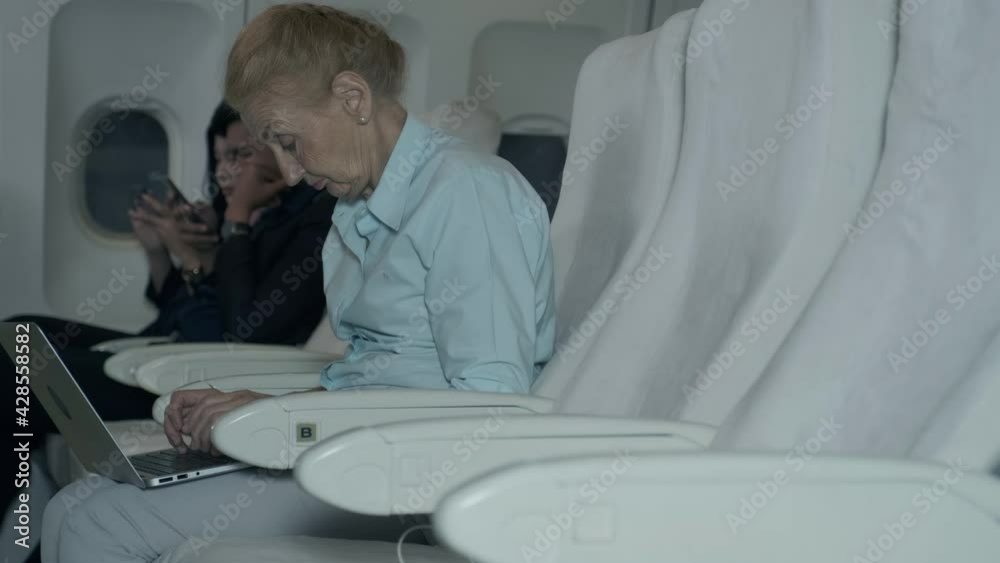 An elderly businessman is using a laptop on the plane before take off. An elderly businessman is using a laptop on the plane before take off.