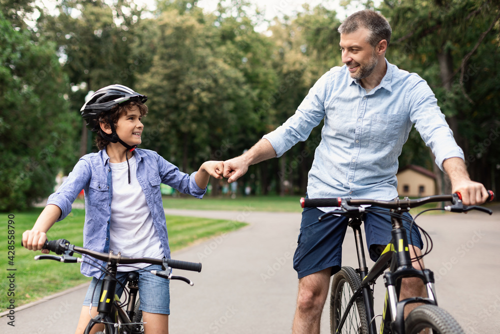 Man giving fist bump to son riding bicycles at park