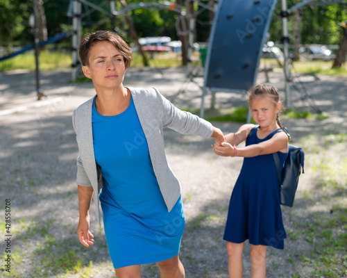 The naughty girl pulls her mother by the hand, wanting to stay on the playground. The capricious daughter resists and does not want to leave.