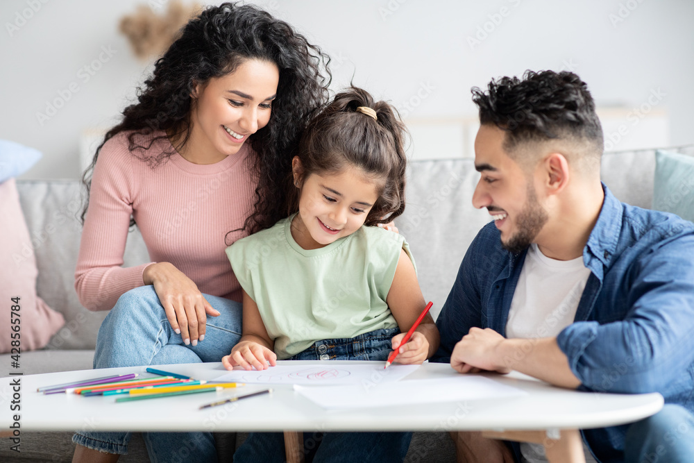 Loving Arab Parents Drawing With Their Little Preschooler Daughter At Home Loving Arab Parents Drawing With Their Little Preschooler Daughter At Home