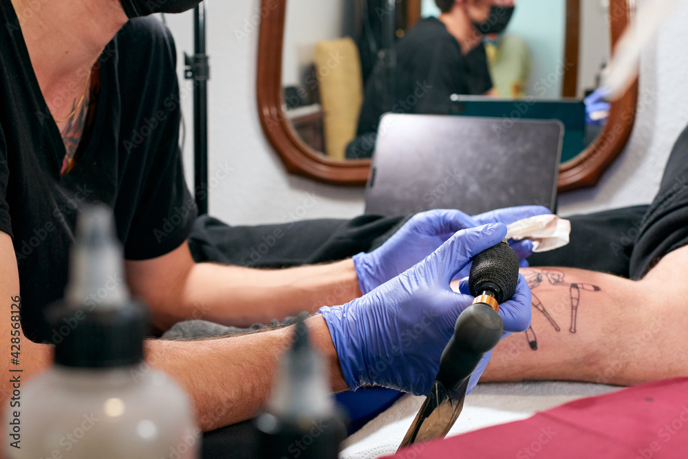 the tattoo artist in blue gloves doing a tattoo on the leg of a male in a studio the tattoo artist in blue gloves doing a tattoo on the leg of a male in a studio