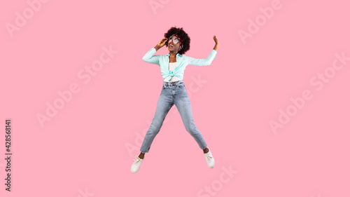 Joyful African Woman Jumping Wearing Sunglasses Posing Over Pink Background