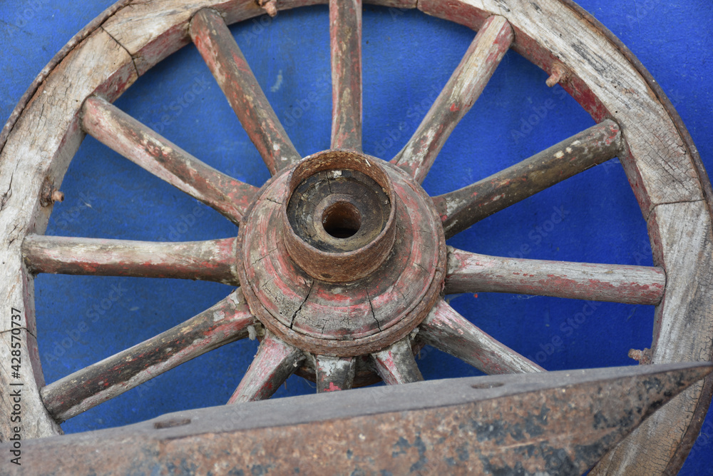 Wooden wheel of an old wagon on a bluewashed wall and antique wrought iron tool in front
