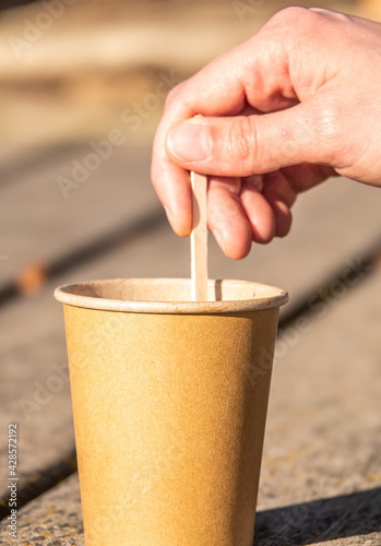 Photography Male hand stirring a stick on a brown paper cup on a wooden surface