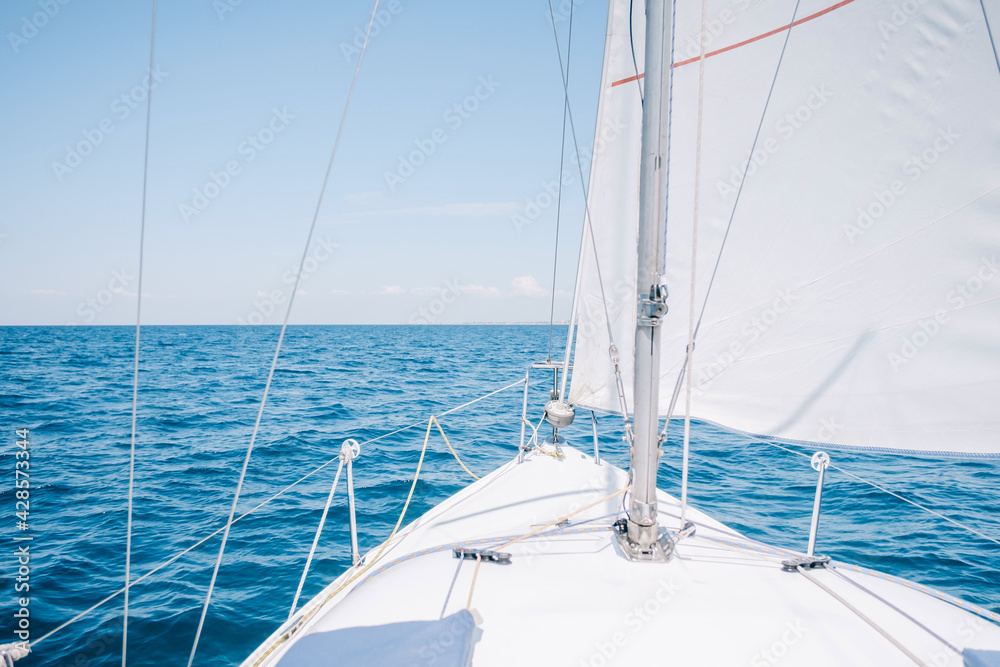 Yacht sailing with sails raised in blue sea on sunny clear day. A view from the deck to the bow. Yacht sailing with sails raised in blue sea on sunny clear day. A view from the deck to the bow.