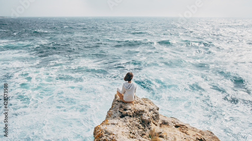 Young woman traveler enjoys the sound of the sea and meditates in the lotus position.