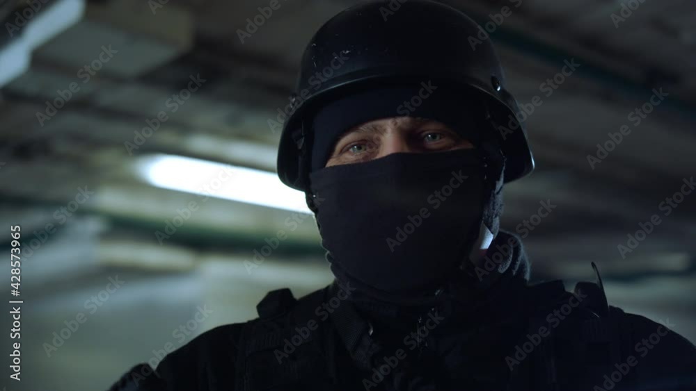 SWAT member standing in dark building. Masked military soldier posing at camera SWAT member standing in dark building. Masked military soldier posing at camera