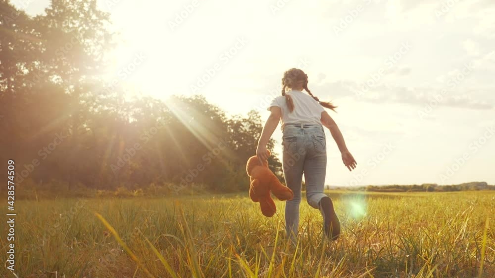 little girl with a teddy bear run in the park on the grass. happy ...