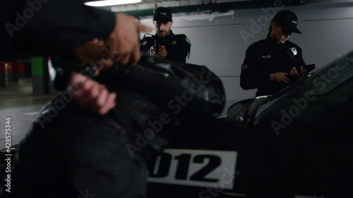 Police team arresting criminal at parking. Cop handcuffing suspect at patrol car