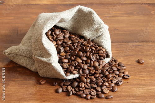 The coffee spilled out of the linen sack. Coffee in a linen bag on a wooden background. 