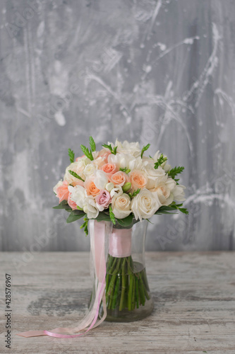 Beautiful bridal bouquet of white and pink flowers and greenery, decorated with long silk ribbon lies on a gray textural background.