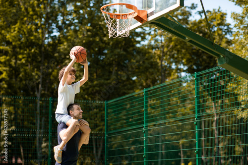 Happy father helps his son to score a basket outdoors photo