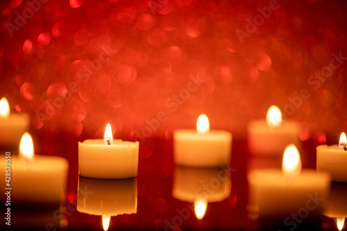 some tee candles on a black acrylic underground  background red illuminated and blurred