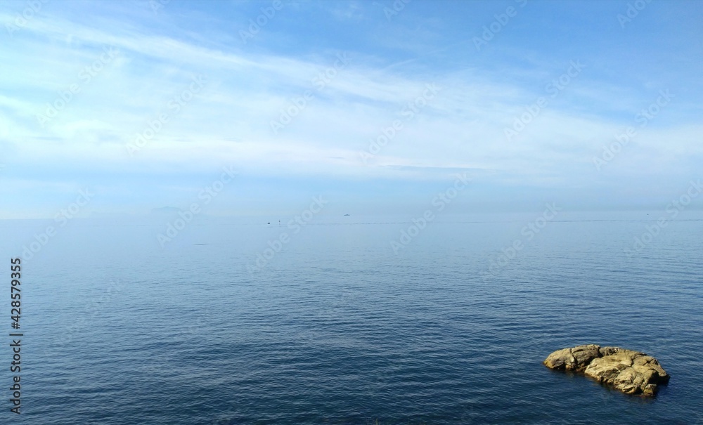Marine panorama a blue expanse where the sea meets the sky with a single orange rock in the foreground Marine panorama a blue expanse where the sea meets the sky with a single orange rock in the foreground