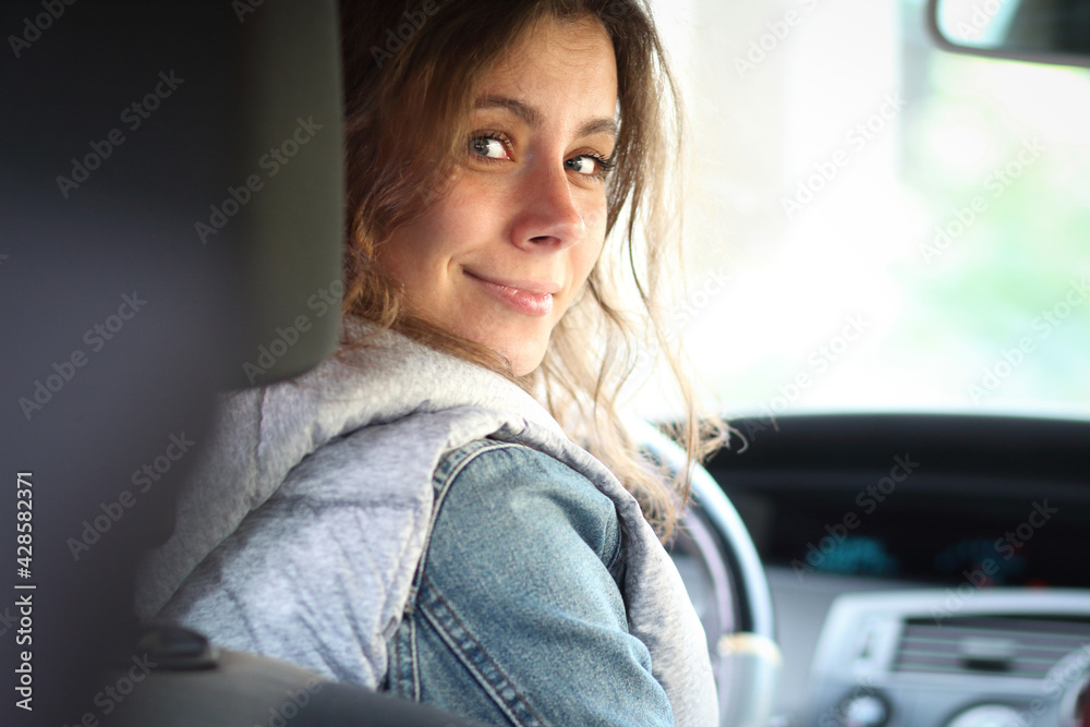 Young woman driver beginner. Girl look back in vehicle interior. Female car driver.