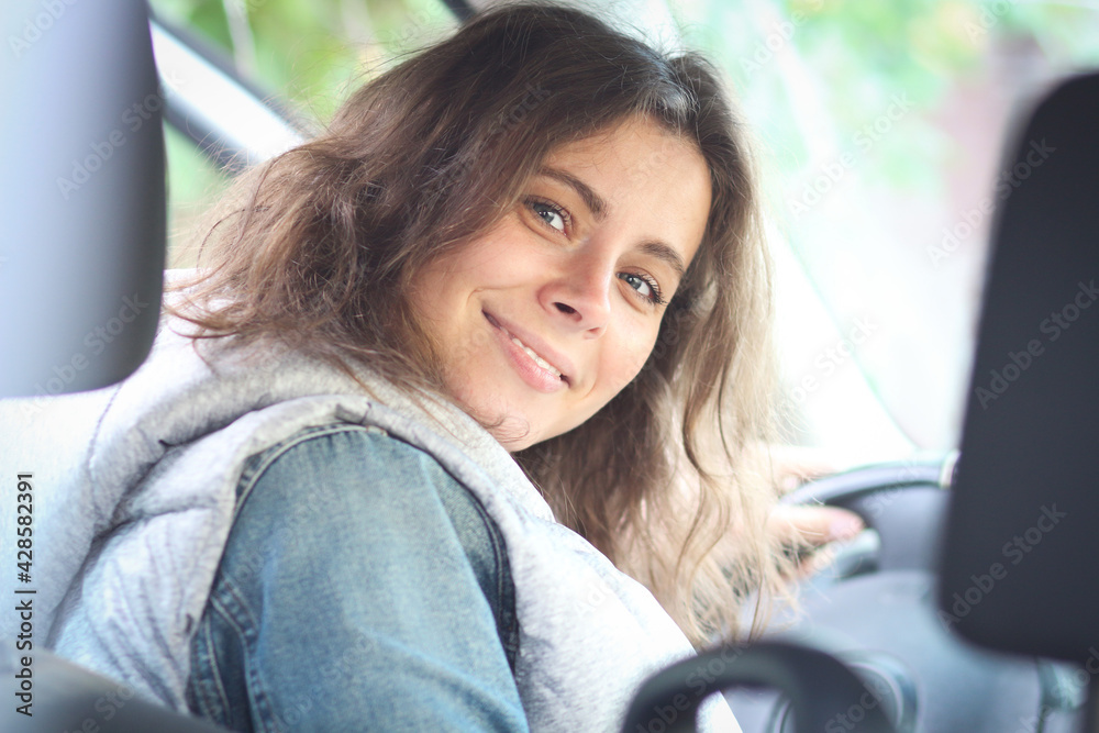 Smiling woman sitting in car and looking back. Female driver.