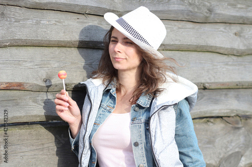 Beautiful woman in white hat with lollipop in-country ferme posing near wooden fence. Cowgirl on ferme.