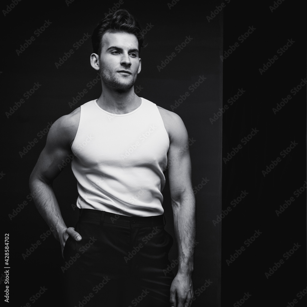 Monochrome portrait of a handsome young man with stylish haircut in a white undershirt and black pants. Studio shot. Monochrome portrait of a handsome young man with stylish haircut in a white undershirt and black pants. Studio shot.