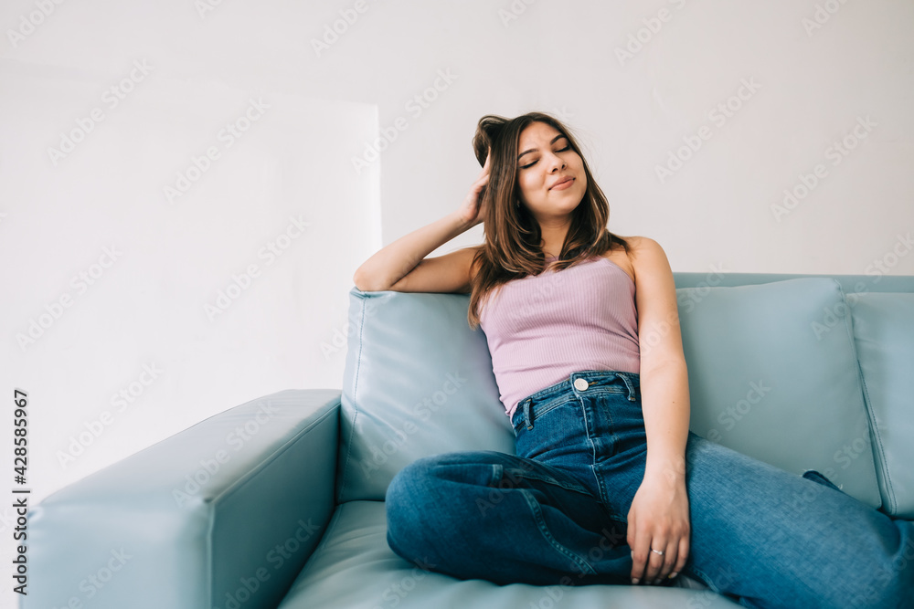 Young calm caucasian woman relaxing, sitting on sofa in modern living room, lazy happy woman resting at home.