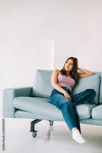 Young calm caucasian woman relaxing, sitting on sofa in modern living room, lazy happy woman resting at home.