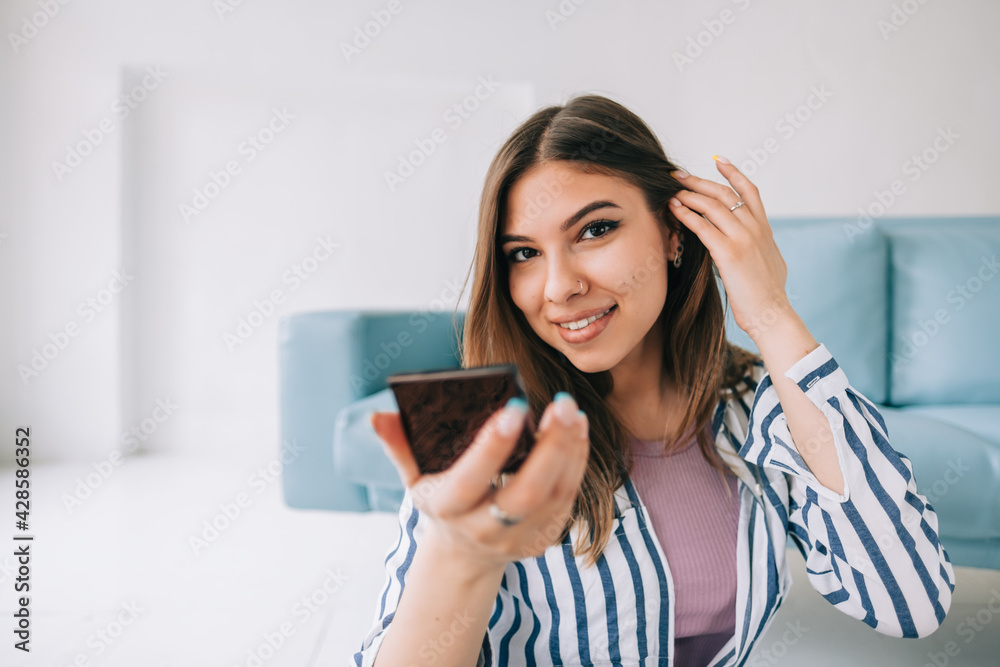 Attractive caucasian young woman holding cosmetic mirror in hand and looking on camera .