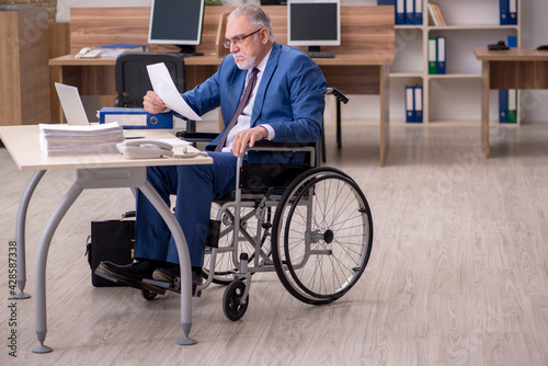 Old businessman employee in wheel-chair working in the office