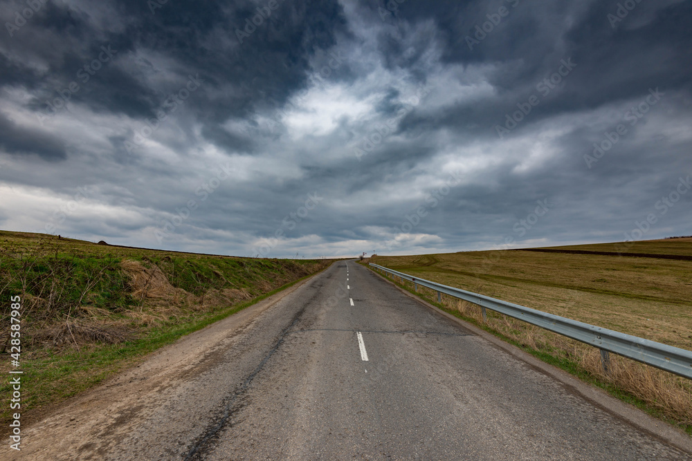 Asphalt road leading to the top of the hill, dramatic gathering stormclouds at spring.