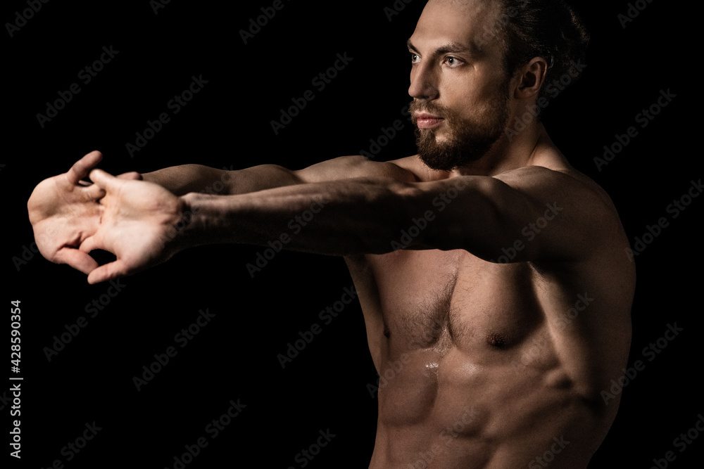 An athletic man doing stretching exercises on a black background An athletic man doing stretching exercises on a black background