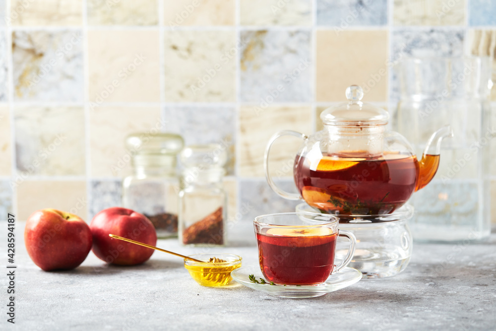 Fruit tea with apples and thyme in glass teapot and cup on the kitchen table Fruit tea with apples and thyme in glass teapot and cup on the kitchen table