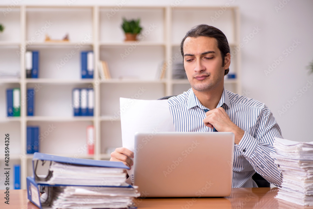 Young male employee unhappy with excessive work in the office Young male employee unhappy with excessive work in the office